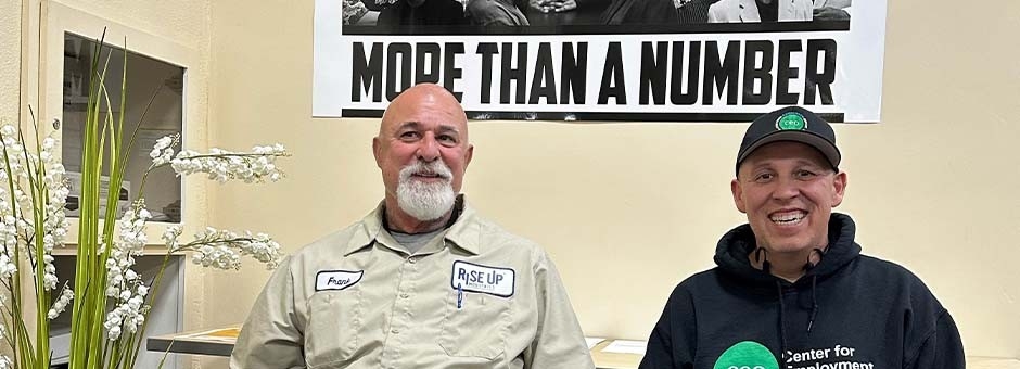 Frankie Perez and colleague sitting in front of a sign that says More Than a Number