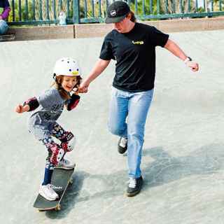 Girl being helped down a steep ramp while on a skateboard